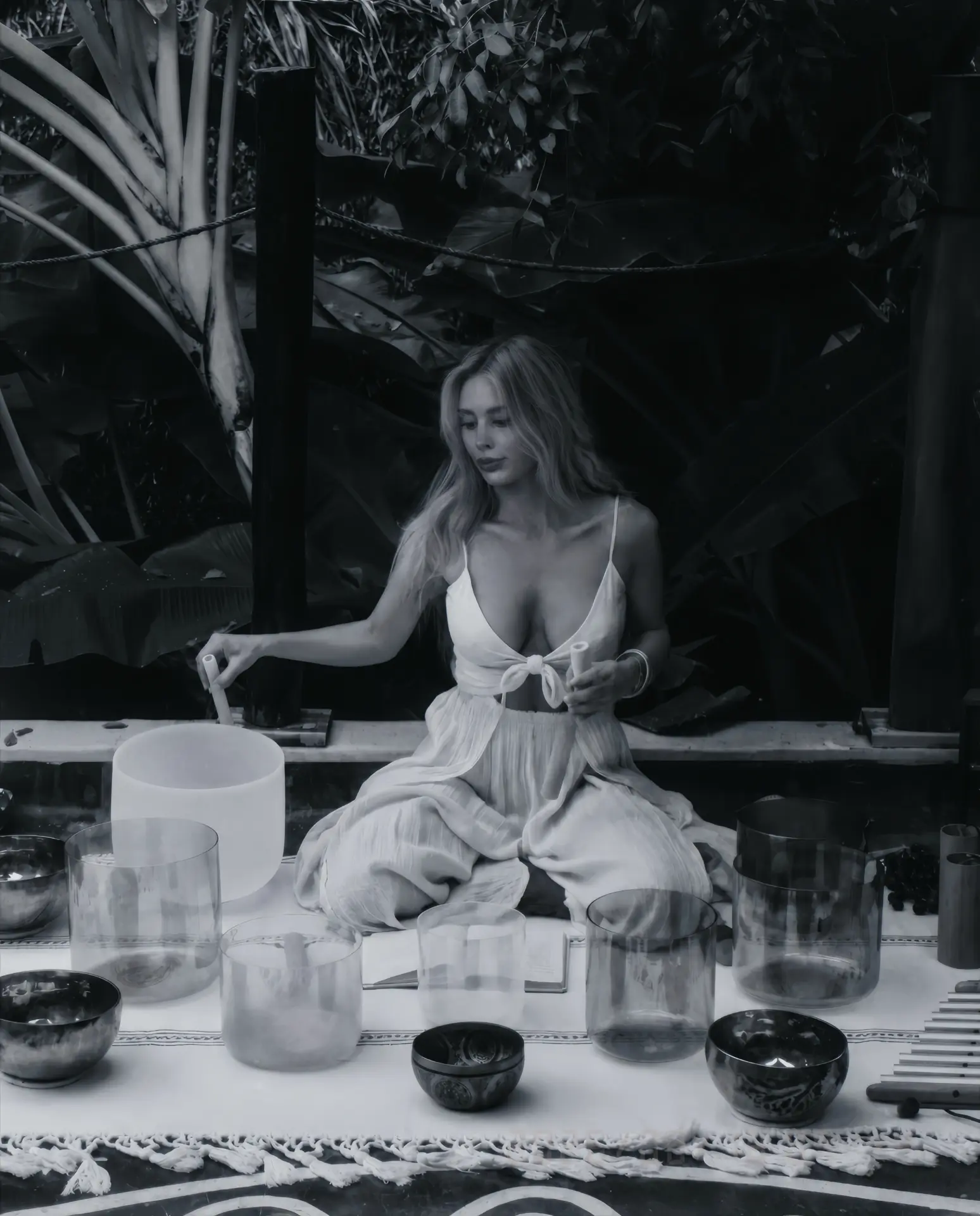 Gia seated with crystal singing bowls in a tropical outdoor setting